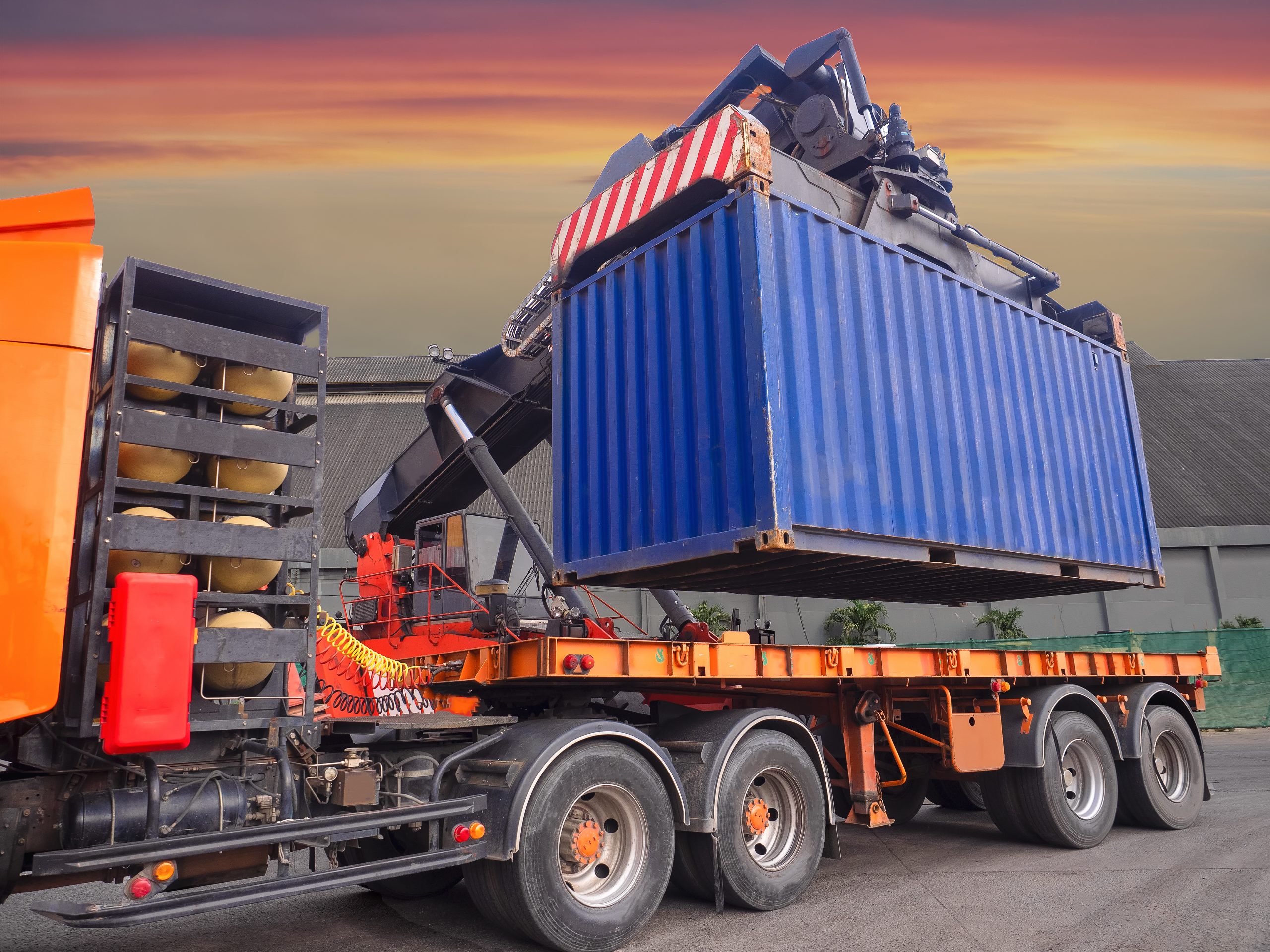 The reach stacker is lifting 20' container from truck to storage area for stuffing cargo in container at industrial warehouse.